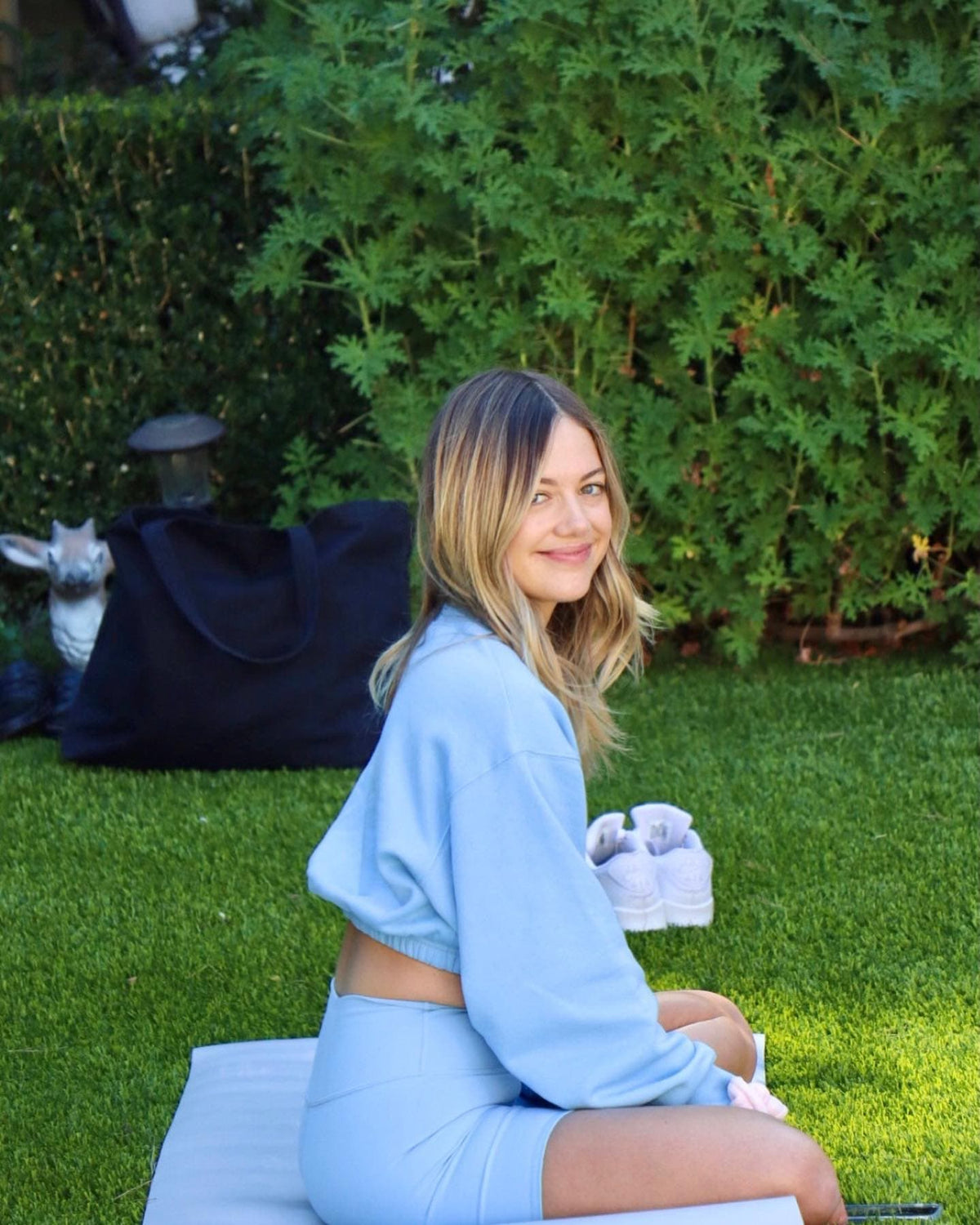 @meetbritt wearing a pair of Tile Blue High Waist Biker Shorts with a matching Devotion Crew Neck Pullover while sitting on a yoga mat in a grass area.